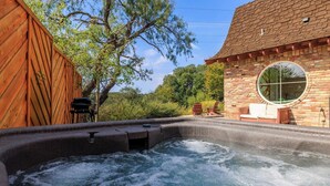 Ein Whirlpool mit Holzterrasse, ein Backsteinhaus mit rundem Fenster und Gartenmöbel.