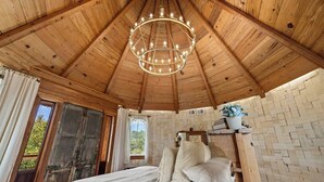 Eine Holzbalkendecke mit einer Kronleuchter, ein Bett mit Kissen, ein Fenster und eine Ziegelwand.
