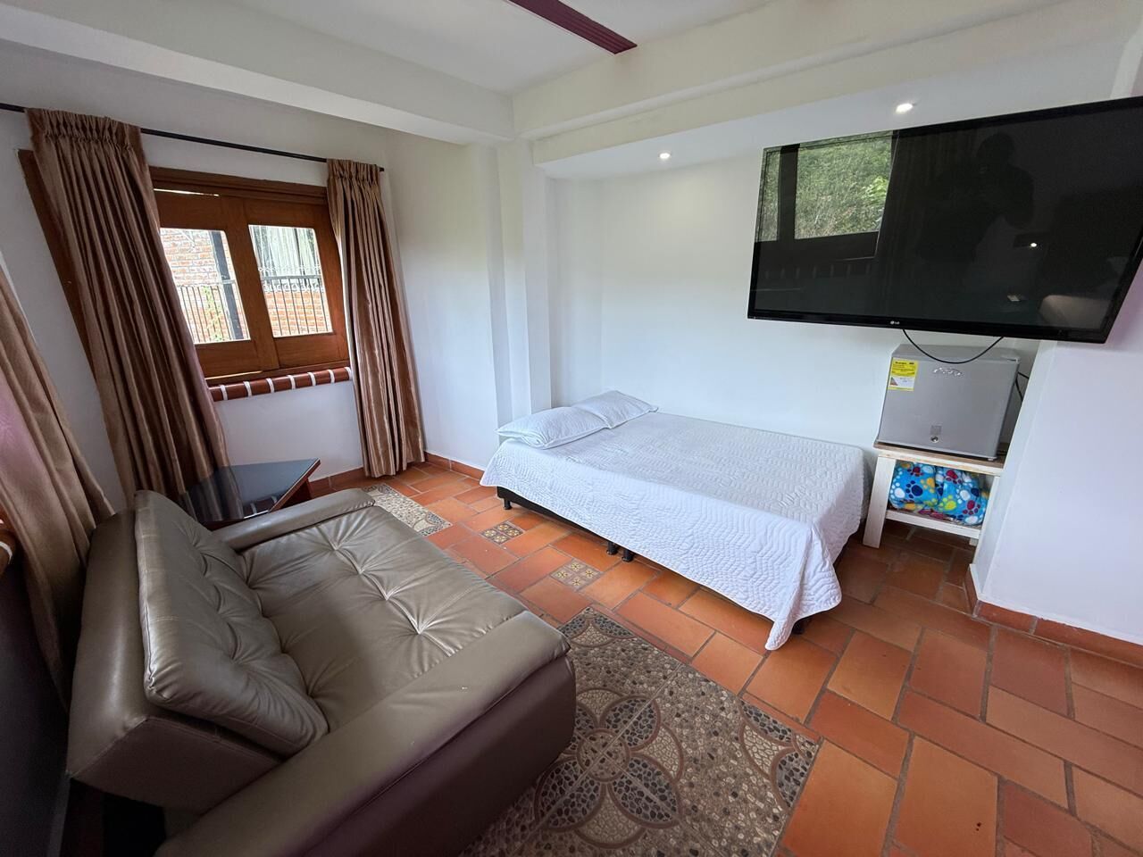 A bedroom with a bed, a sofa, a television, and a small refrigerator.