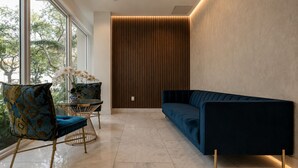 Ein modernes Interieur mit einem dunkelblauen Sofa, einem gemusterten Sessel, einem kleinen runden Tisch mit einem Blumenstrauß und einer hohen Holzwand.