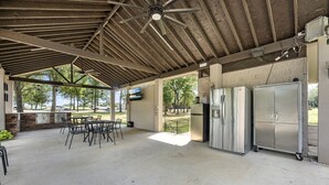 Eine überdachte Terrasse mit Tisch, Stühlen, einem Deckenventilator und zwei großen Kühlschränken.