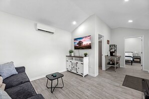 Una sala de estar moderna con un sofá gris, una mesita negra pequeña, un armario blanco y un televisor fijado en la pared.