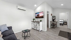 Ein modernes Wohnzimmer mit einem grauen Sofa, einem kleinen schwarzen Tisch, einem weißen Schrank und einem an der Wand befestigten Fernseher.