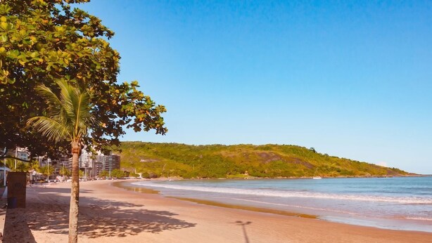 Ein Strand mit blauem Himmel, sandigem Ufer und einer Hügelkette im Hintergrund.