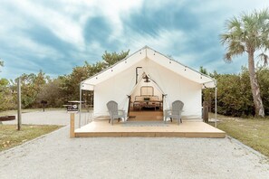 A tented accommodation with a wooden deck, two chairs, and a bed inside.