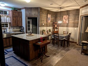 Uma cozinha com armários de madeira, bancada de granito, área de refeições com mesa e cadeiras, e luminária pendente.