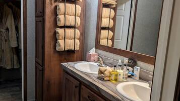 A bathroom with wooden cabinets, a double sink, and a mirror with lights.