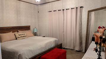 A bedroom with a bed, a nightstand, a red bench, a ceiling fan, a mirror, and curtains.
