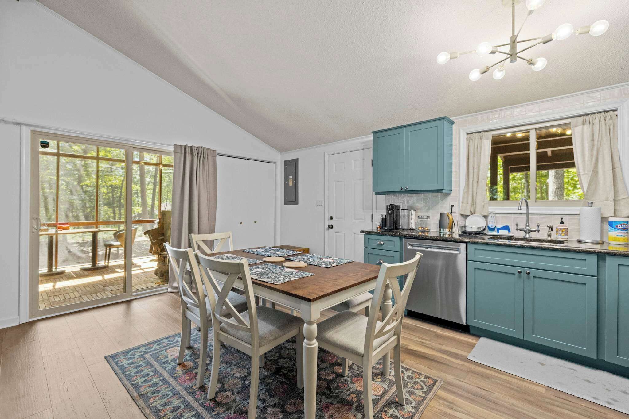A kitchen with teal cabinets, a wooden dining table with chairs, a coffee maker, and a window with curtains.