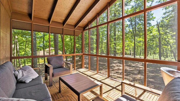 A wooden deck with a sofa, chairs, and a table, overlooking a forest.