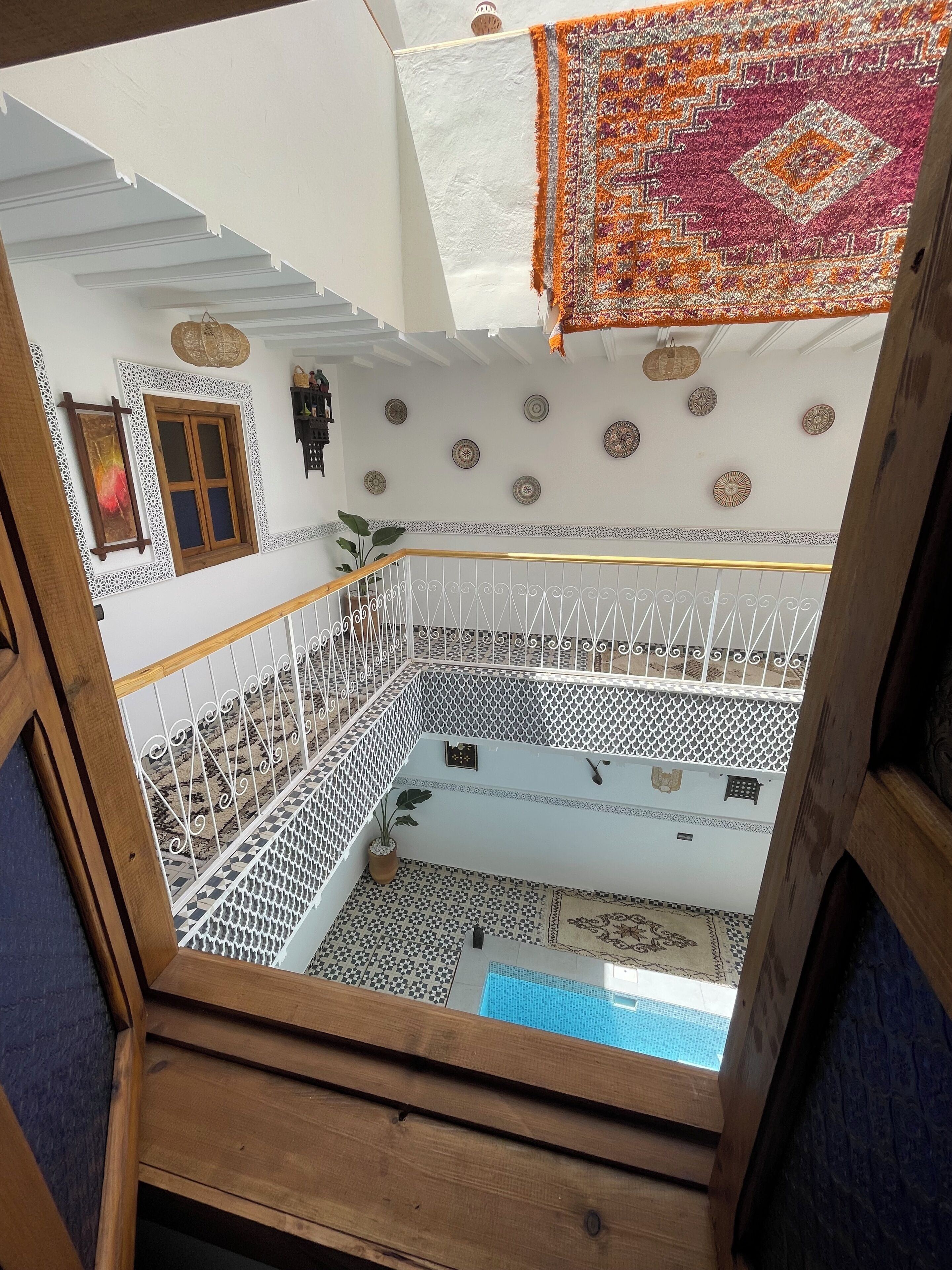 Un interior de varios niveles con balcón, baldosas estampadas y placas decorativas en la pared.