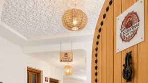 Een hotel lobby met een receptiebalie, een houten deur met een bordje, een patroon vloer en een hangende lamp.