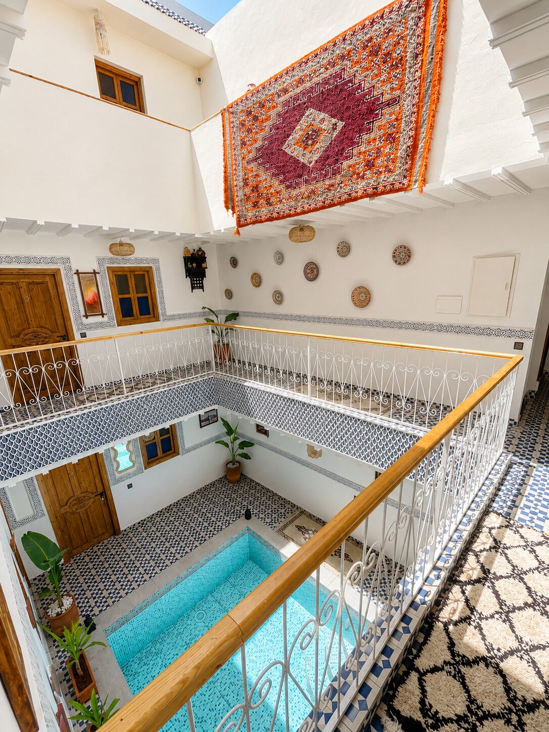 Une cour intérieure à plusieurs niveaux, avec une piscine, une porte en bois et un tapis à motifs.