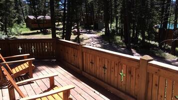 A wooden deck with chairs, a wooden fence, and a forested area in the background.