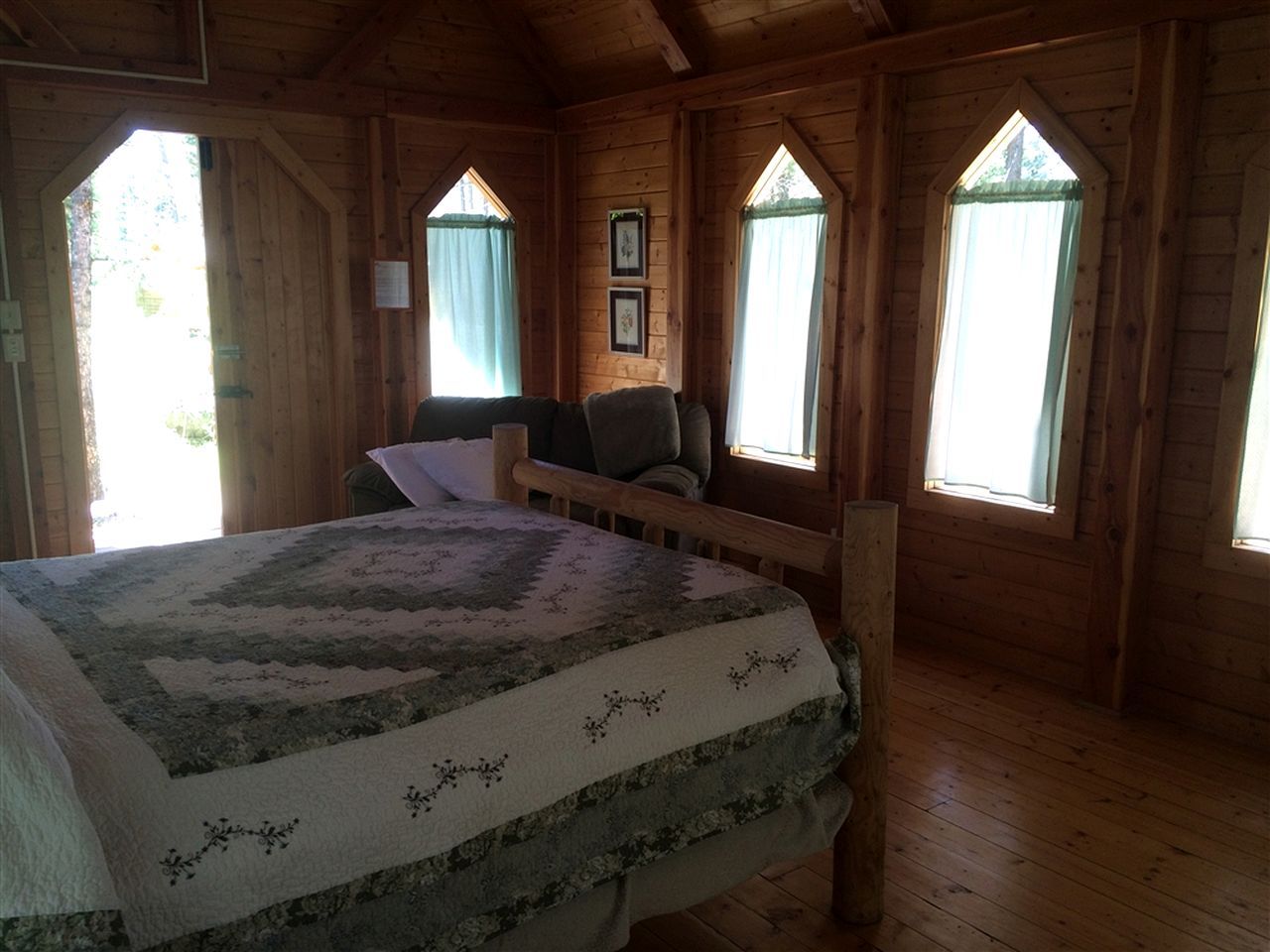 A wooden cabin bedroom with a bed, a bench, and two windows.