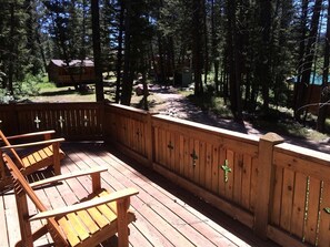Une terrasse en bois avec des chaises, une clôture en bois et une zone boisée en arrière-plan.
