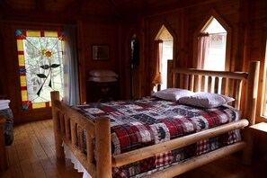 A wooden-framed bed with a plaid quilt, a stained glass window, and a wooden headboard. - Romantic Cabin Rental for Couples in Secluded Woodlands near Butte, Montana (Hall)