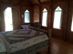 Une chambre dans une cabane en bois, avec un lit, un banc et deux fenêtres.