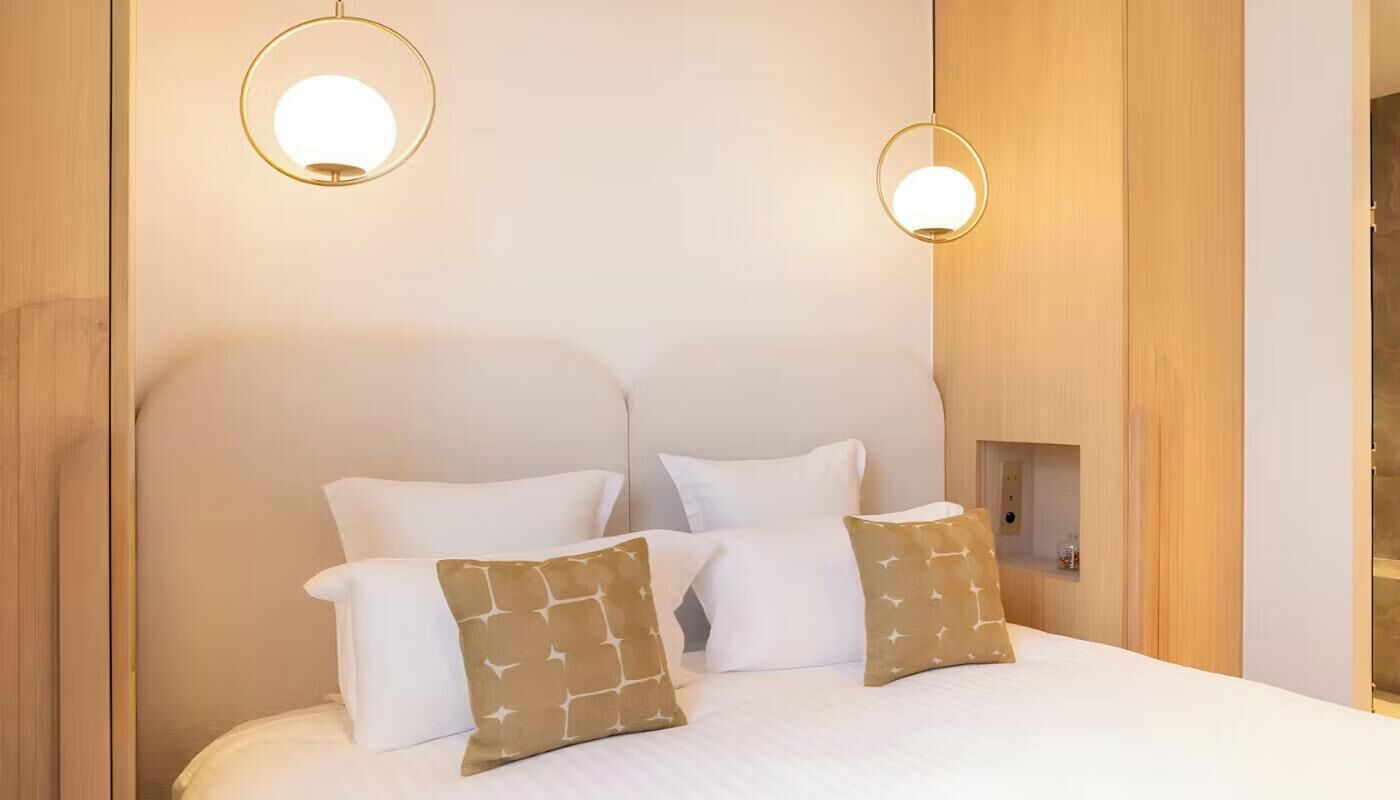 Una habitación de hotel con una cama, dos luces fijadas a la pared y un cabecero de madera.