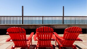 A wooden deck with three red Adirondack chairs facing a wooden railing overlooking the ocean. - Beachfront Escape with Breezy Views in North Truro, Massachusetts (North Truro)
