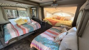 Un intérieur de camping-car confortable avec deux lits, une petite table et un espace de couchage aménagé sous une tente.