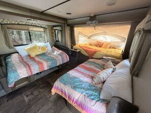 Ein gemütliches Wohnmobil-Interieur mit zwei Betten, einem kleinen Tisch und einem schlafbaren Zeltbereich.