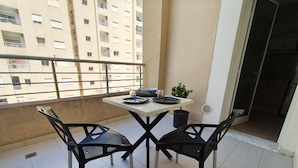 Un balcon avec une table et deux chaises, un pot de fleurs et une vue sur un immeuble.