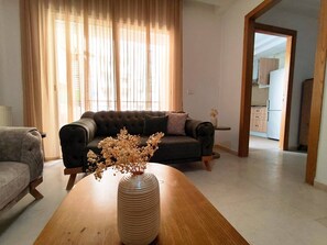 A living room with a sofa, a wooden coffee table with a vase, and a view into the kitchen. - Superb Cozy 1-bedroom Apartment in Jardins de Carthage (Tunis)