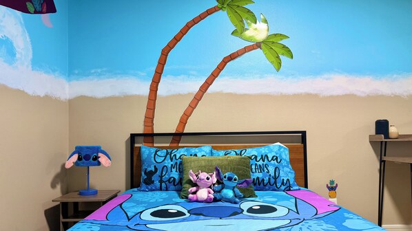 Una camera da letto con un murale a tema spiaggia, un letto con copripiumino a fiori blu e un comodino con una lampada.