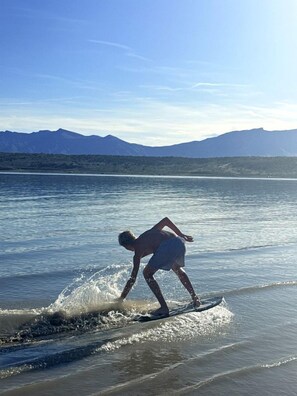 Une personne fait de la planche à voile sur une plage, avec des montagnes en arrière-plan.