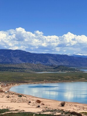 Un lac avec des montagnes en arrière-plan, un ciel dégagé et quelques bâtiments près du rivage.