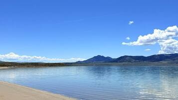 A beach with clear water, a sandy shore, and distant mountains under a blue sky.
