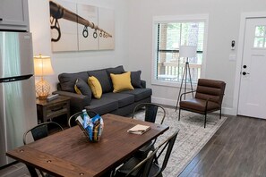 A modern kitchen with a refrigerator, a dining table with chairs, a sofa with cushions, a window with blinds, and a door with a keypad lock. - Pet-Friendly Waterfront Cabin with Loft Interior in Livingston, Texas (Livingston)