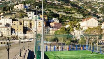Ein Tennisplatz mit Netz, umgeben von einem grünen Zaun, mit Gebäuden im Hintergrund.