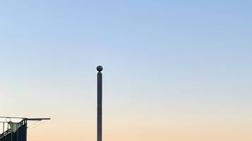 A tall, narrow structure with a spherical top, overlooking a coastal cityscape with buildings and the sea.