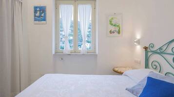 A bedroom with a bed, a window with curtains, a wall-mounted light, and a small table with a decorative item.
