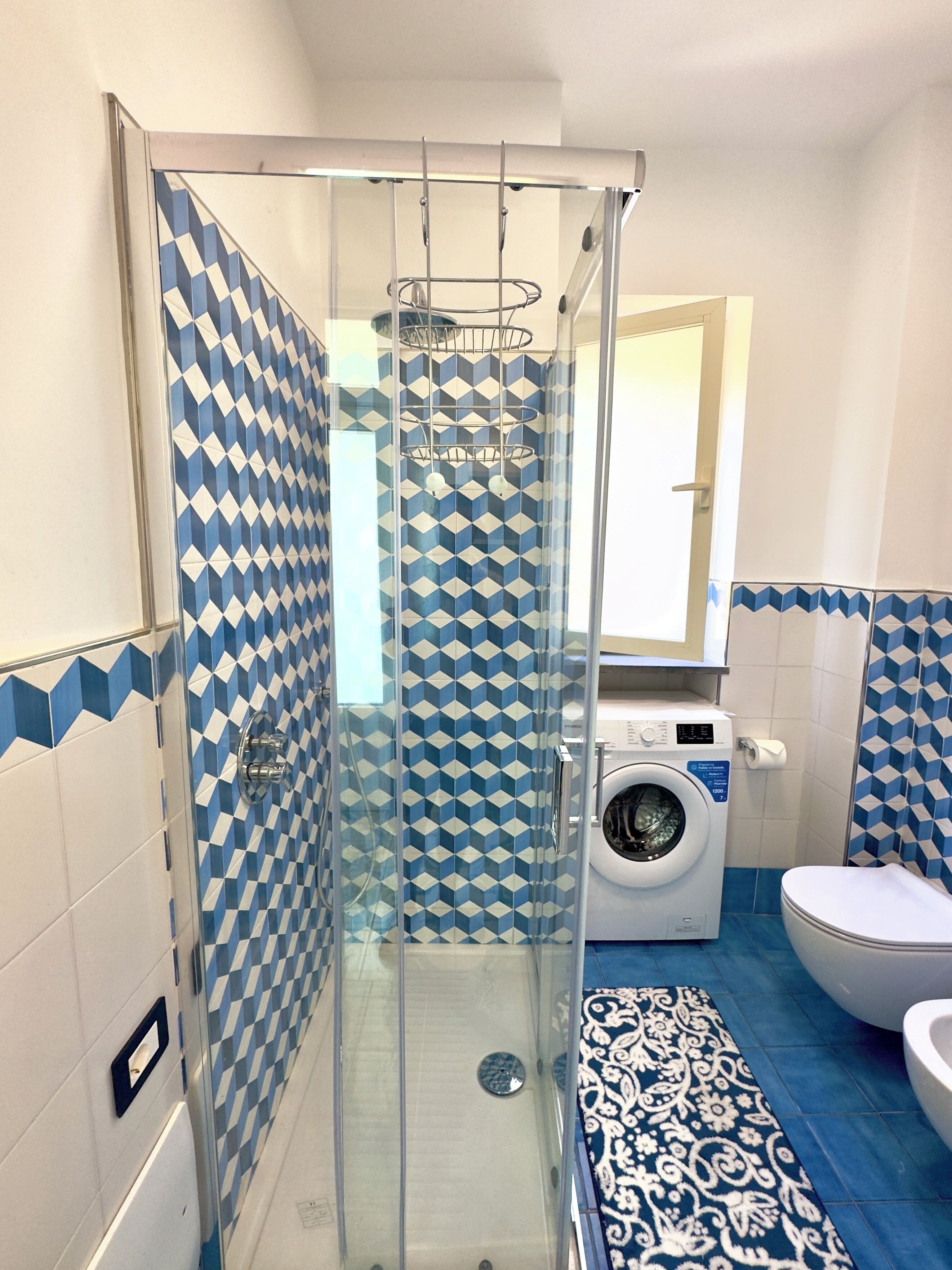 A bathroom with a glass-enclosed shower, a washing machine, and a toilet.