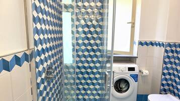 A bathroom with a glass-enclosed shower, a washing machine, and a toilet.