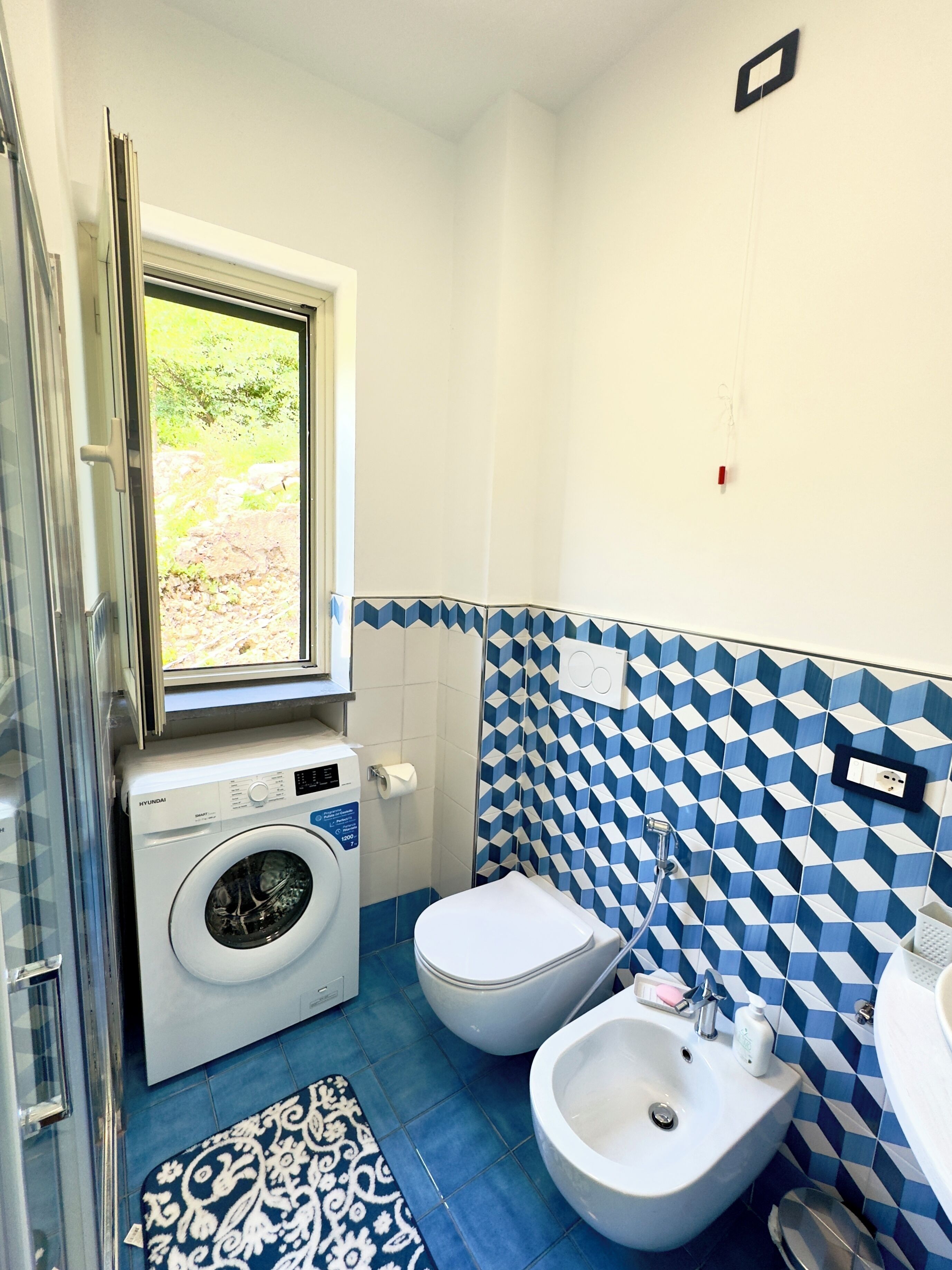 A compact bathroom with a washing machine, toilet, bidet, and sink.