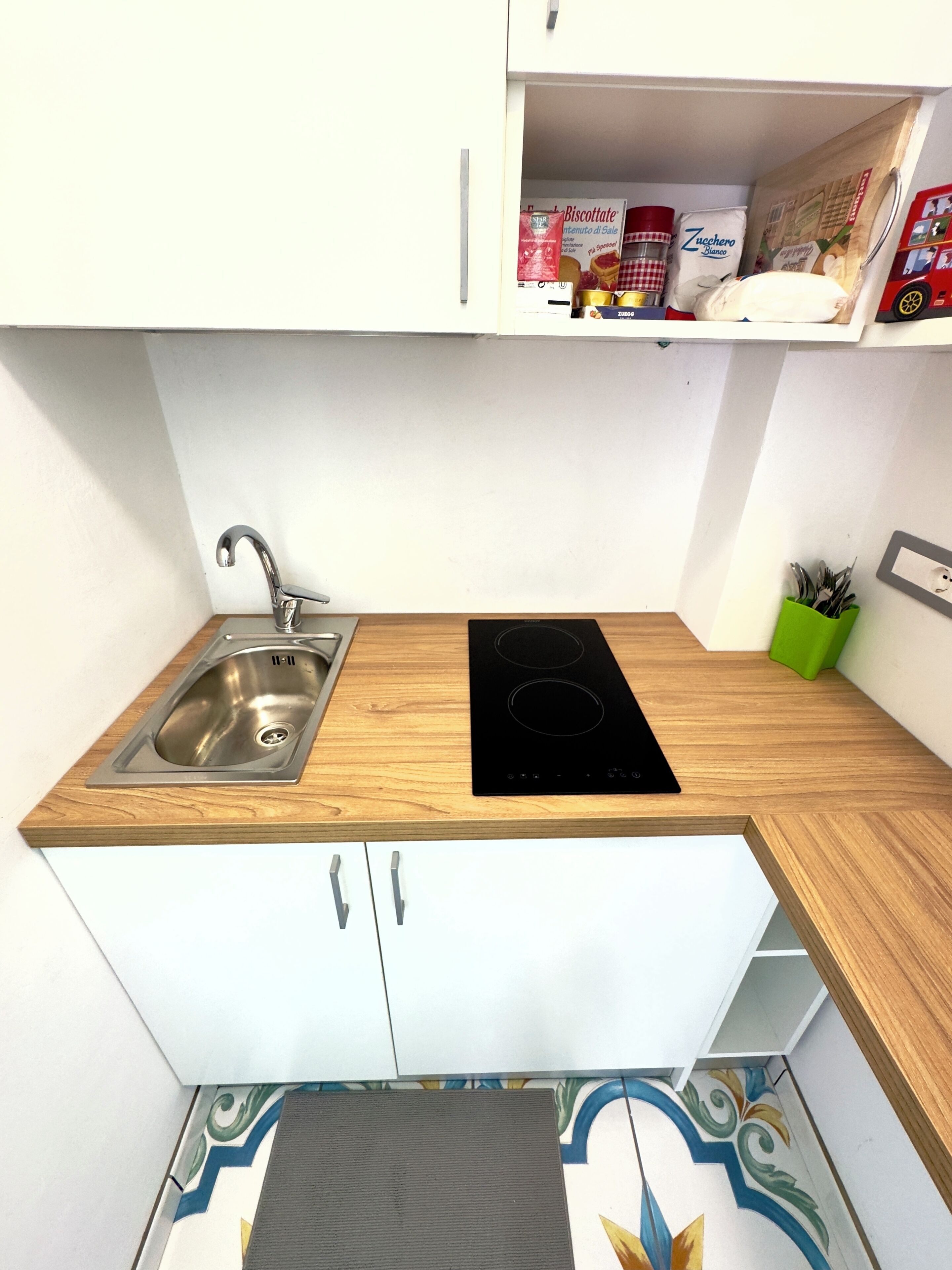 Een praktische keuken met een spoelbak, een zwart inductiefornuis en een klein kastje boven het aanrecht.