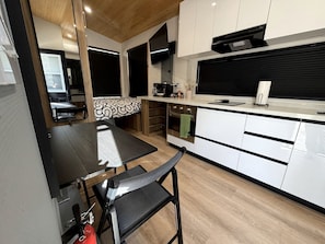A modern kitchen with a dining table and chairs, a TV mounted above the counter, and a built-in oven.