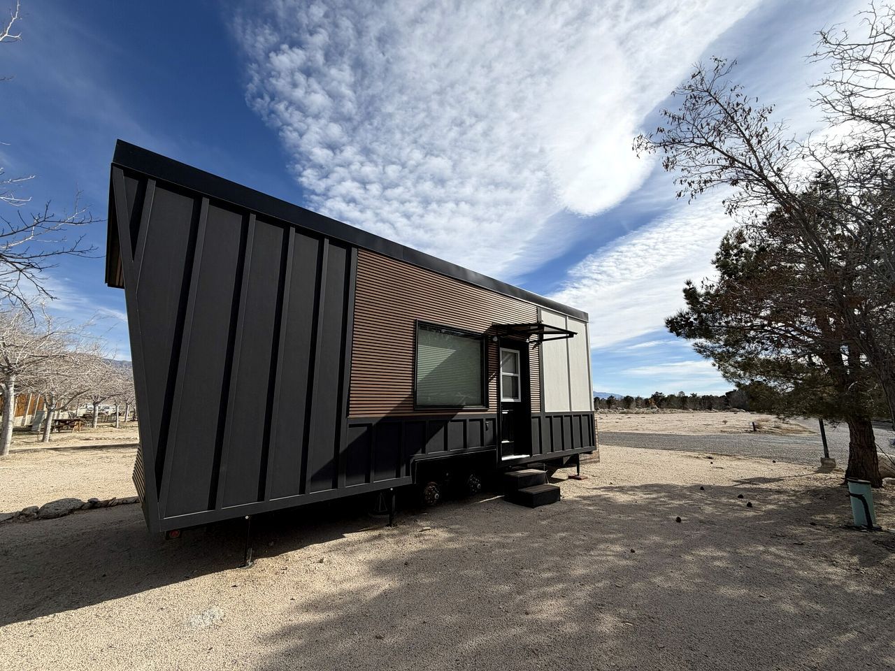 Una casa móvil moderna de un piso, con techo plano, un ventanal grande y un pequeño porche.