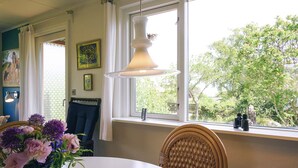 A dining area with a round table, wicker chairs, a vase of flowers, a hanging lamp, and a window with a view of greenery. - 5 Person Holiday Home in Allinge (Allinge)