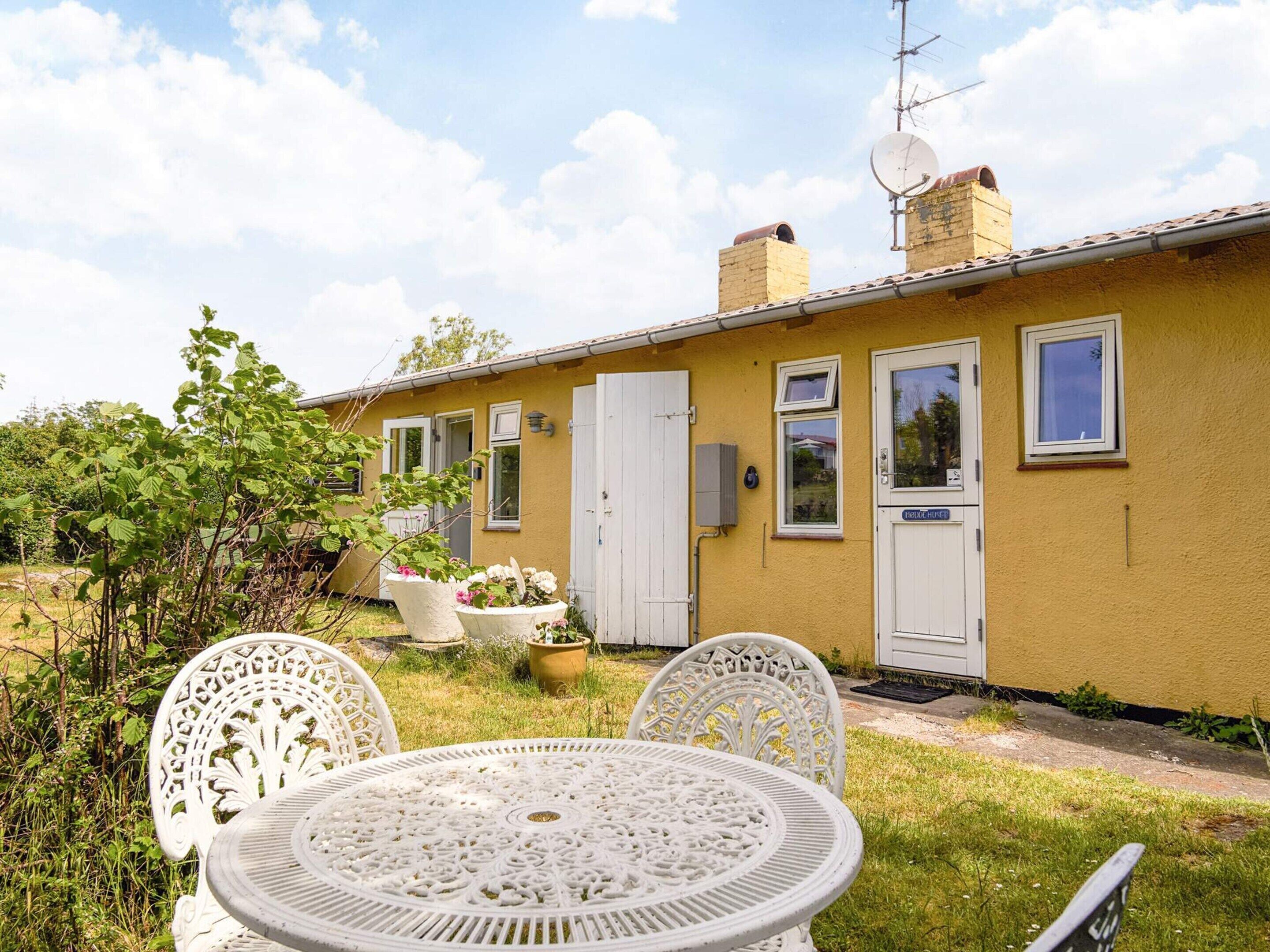 A yellow house with a white door, a satellite dish, and a small garden with a table and chairs.