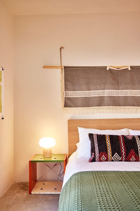 Une chambre à coucher avec un lit, une table de chevet avec une lampe, une tapisserie murale et un coussin décoratif à motifs.