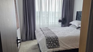 Ett hotellrum med en säng, en bordsfläkt och utsikt genom fönstret.