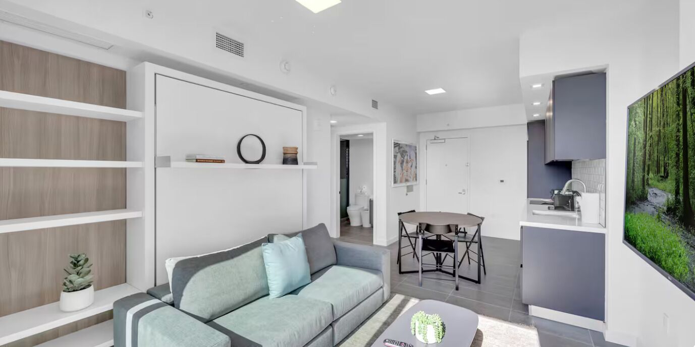 A modern living room with a sofa, a dining table, and a kitchen area with a large window.