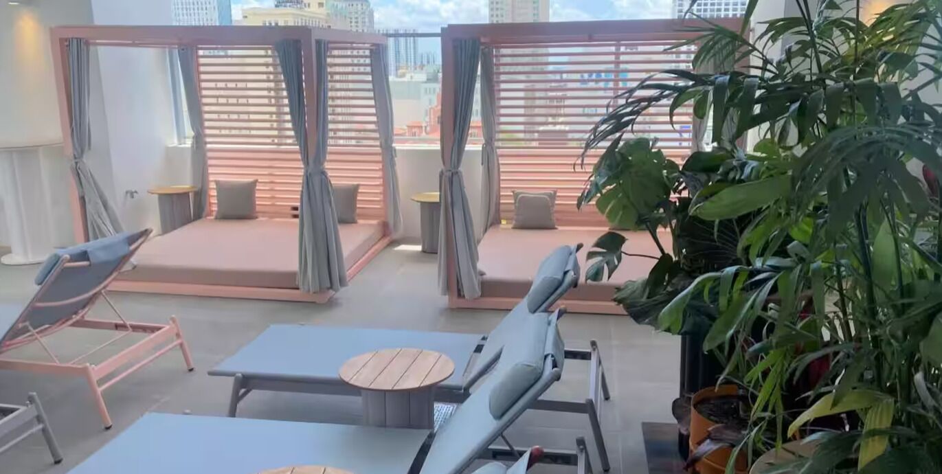 A balcony with lounge chairs and tables, a potted plant, and a view of buildings.
