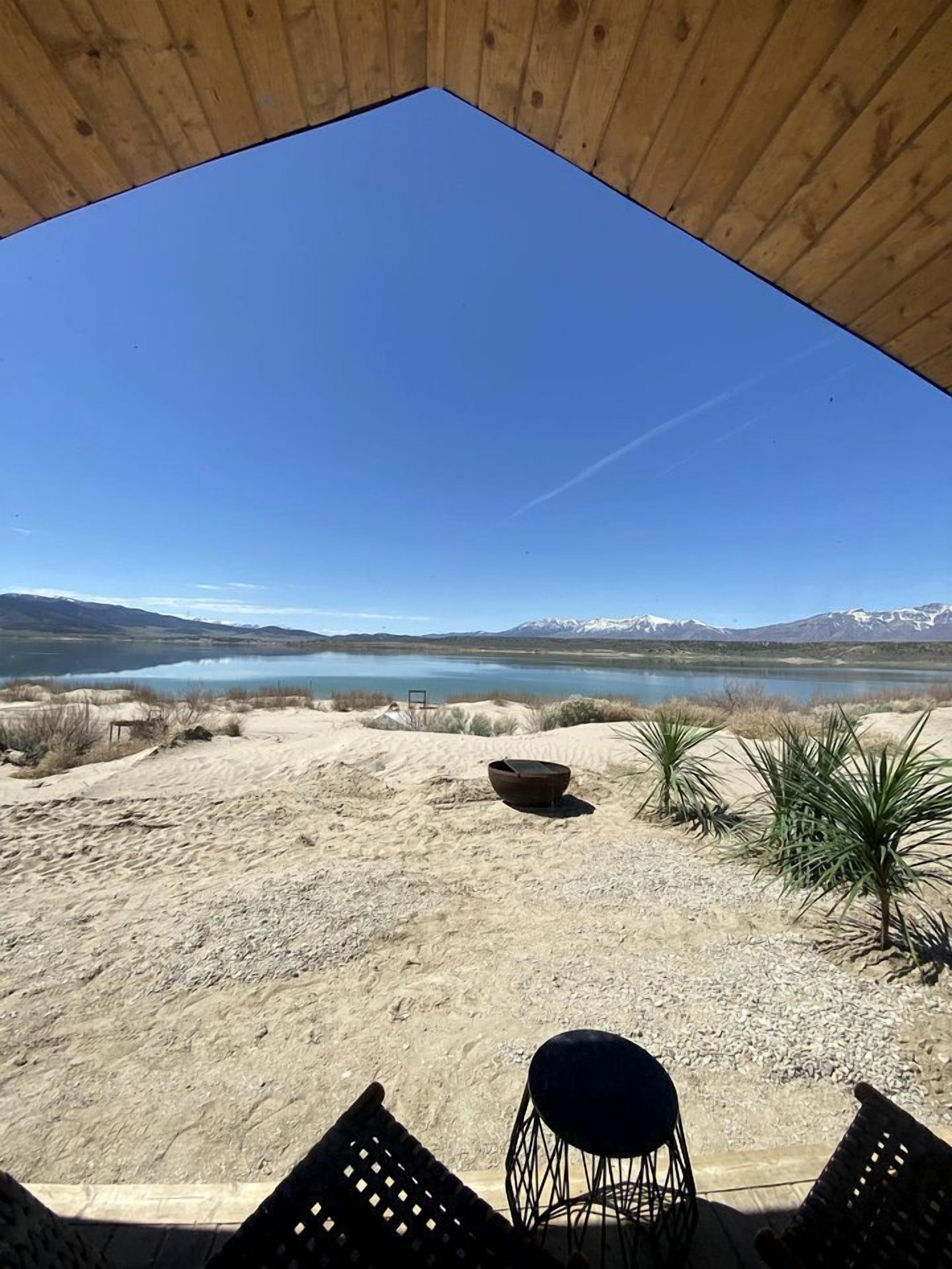 A covered outdoor area with a view of a lake and mountains, featuring a seating area with chairs and a table.