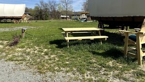 Una mesa de picnic y un espacio cubierto en un campo cubierto de hierba, con un edificio al fondo.